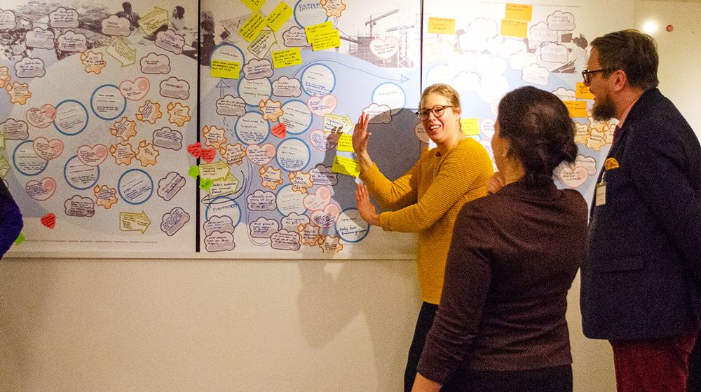 Woman pointing on a whiteboard while two others watch.